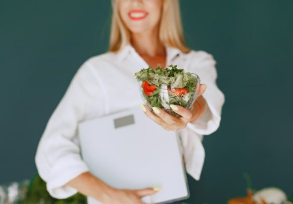 A woman with a vibrant smile offering a fresh salad bowl, promoting healthy eating.